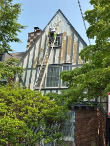 Tudor-style house renovation with worker painting exterior walls.