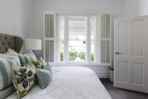 Bright bedroom featuring a large window with white shutters and a neatly made bed.